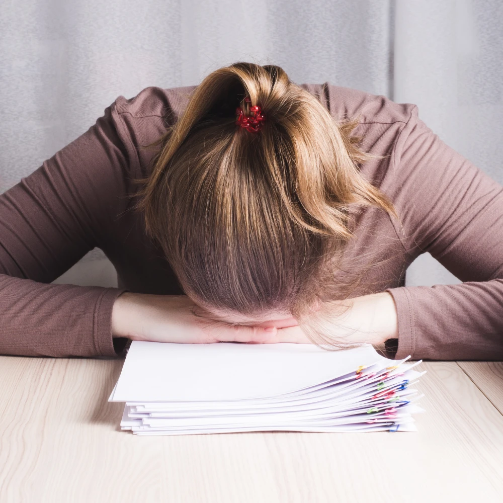 A frustrated woman with her head down on a stack of papers